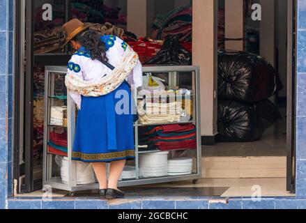 Ecuadorian indigenous Otavalo woman in traditional clothing shopping in textile fabric shop, Otavalo, Ecuador. Stock Photo