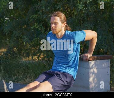 Sportive guy training triceps while doing push ups on bench in park on summer day Stock Photo