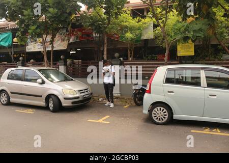 GEORGETOWN, MALAYSIA - Feb 02, 2020: A closeup shot of a dark skinned man using his smartphone between parking cars in Malaysia Stock Photo