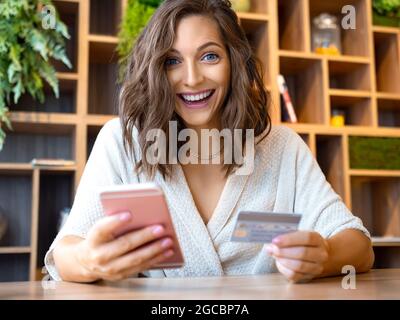 Portrait of a young woman with a smartphone and a credit card. She smiles happily and looks into the camera. Online shopping and sales concept. Stock Photo