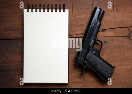 Suicide note, murder investigation. Blank notepad and pistol gun on wooden table background, top view. Copy space template Stock Photo