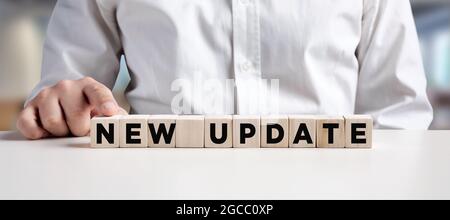 Businessman pressing his finger on the wooden cubes with the word new update. Download a new software or technology update concept. Stock Photo