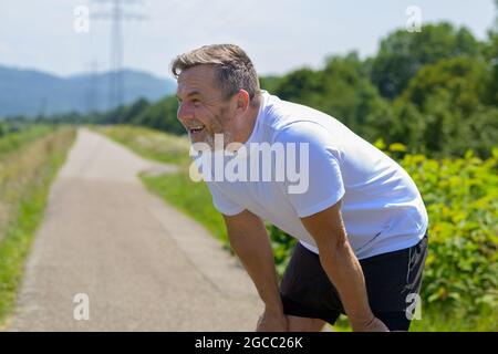 Middle-aged man pausing for a break to catch his breath while out jogging along a rural footpath on a lovely sunny day in a health and fitness and act Stock Photo