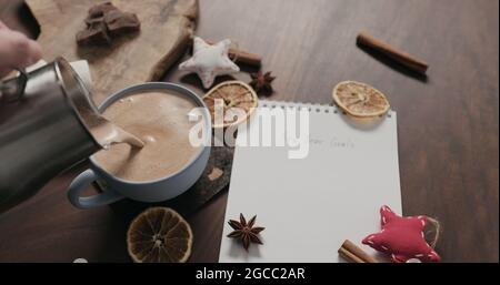 pour hot chocolate into blue cup with new year goals list in notepad, wide photo Stock Photo
