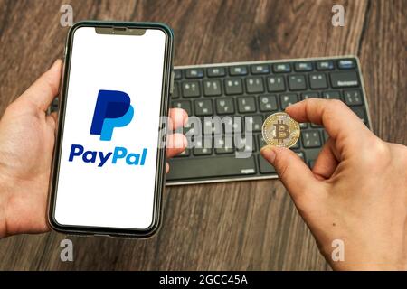 Tashkent, Uzbekistan - April 2, 2021: Hand holds a smartphone with PayPal logo and bitcoin. Symbol of bitcoin cryptocurrency rolling out by online Stock Photo
