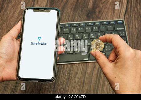 Tashkent, Uzbekistan - April 2, 2021: Hand holds a smartphone with Transferwise logo and bitcoin. Symbol of bitcoin cryptocurrency rolling out by Stock Photo