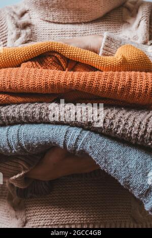 Cropped shot of a female holding knitted warming sweaters. Preparing clothes for coming cold season. Knitted warm pullovers in hands of young woman Stock Photo