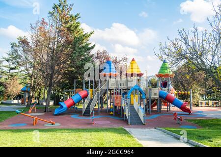 Children playground in public park at sunny day. Colorful swings, seesaw and slides. Stock Photo