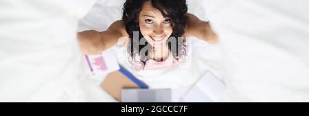Portrait of smiling woman on bed with laptop and business charts Stock Photo