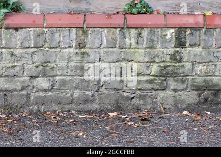 Old grey weathered brick wall with terracotta tiles on top Stock Photo