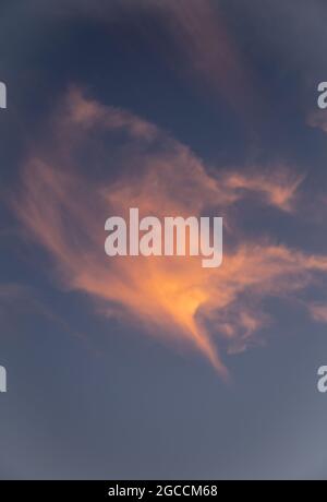 Dramatic storm clouds illuminated by warm golden sunset light against moody blue sky Stock Photo