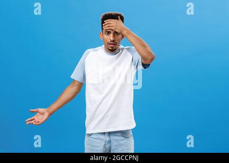 Portrait of intense bothered and irritated dark-skinned male with beard and afro hairstyle holding hand on forehead frowning shrugging feeling Stock Photo