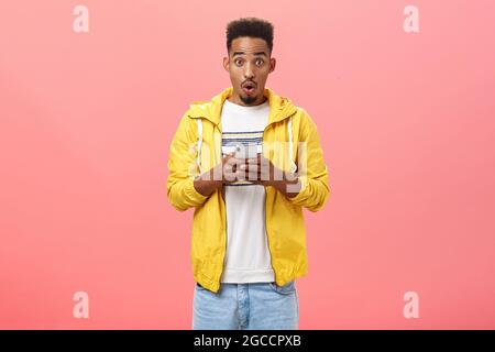 Impressed enthusiastic african american male with curly haircut folding lips in wow sound holding smartphone being excited and thrilled with cool Stock Photo