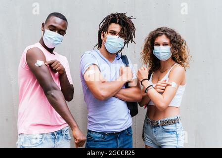 african, latin american and caucasian friends showing arms with a piece of cotton. Concept of Covid vaccination program Stock Photo