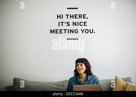 Female professional with laptop looking away and smiling. Cheerful freelancer using laptop while sitting on sofa. Stock Photo
