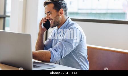 Happy freelancer calling client on mobile phone at office desk. businessman sitting and looking happy while talking on smart phone in office. Stock Photo