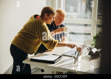 Two colleagues discussing the project in the office over a laptop. businessman and woman discussing as they look at a laptop on a desk in front of the Stock Photo