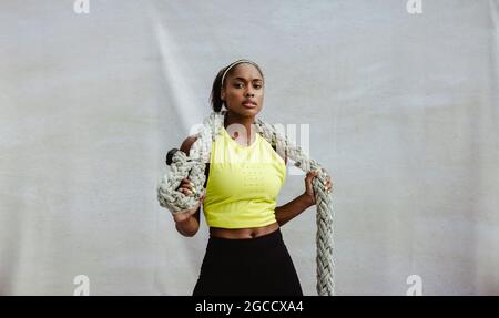 Fit African woman in exercise outfit standing with battle rope. Confident athlete woman holding battling rope. Stock Photo