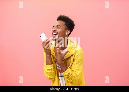 Singing from bottom of heart along favorite music listening song in wireless earbuds with closed eyes and joyful smile gesturing passionately making Stock Photo
