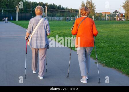 Nordic walking with sticks. Pensioners take care of their health. Evening walk along the street. Grandmothers train muscles. Women are walking in the Stock Photo