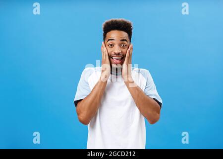 Guy being so delighted and surprised loosing speech. Portrait of charming happy dark-skinned male with afro hairstyle gasping smiling broadly holding Stock Photo