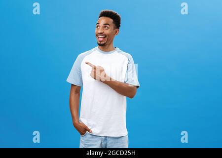 Studio shot of friendly joyful and emotive handsome dark-skinned bearded guy with afro haircut pointing and looking left with excited thrilled face Stock Photo