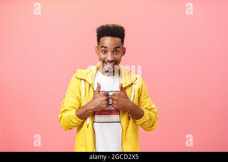 Energetic pleased and delighted african american male with beard and afro hairstyle in stylish yellow jacket raising thumbs up in like gesture and Stock Photo