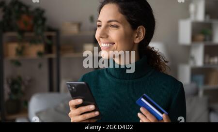 Close up dreamy smiling woman holding smartphone and credit card Stock Photo
