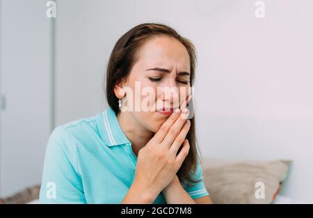 Caucasian woman sitting at home and suffering from toothache. Stock Photo