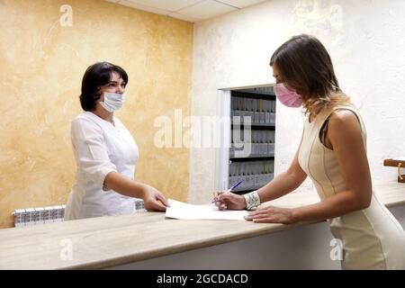 Client Signing Paper At Reception Desk In Face Mask Stock Photo