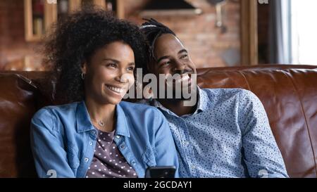 Happy ethnic couple rest on sofa dreaming visualizing Stock Photo