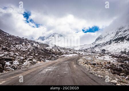 isolated tarmac road with snow cap mountain background and amazing sky at morning image is taken at sela pass tawang arunachal pradesh. Stock Photo