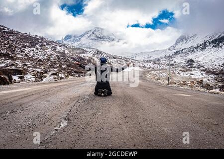 man solo traveler at isolated tarmac road with snow cap mountains in background at morning image is taken at sela pass tawang arunachal pradesh india. Stock Photo