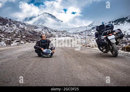 man solo traveler at isolated tarmac road with snow cap mountains in background at morning image is taken at sela pass tawang arunachal pradesh india. Stock Photo