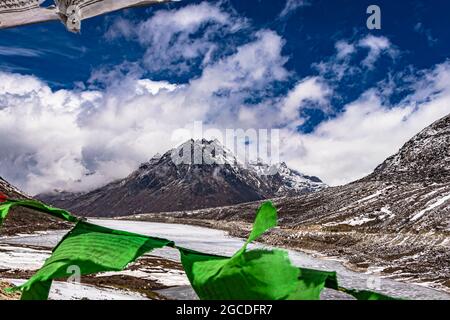 snow cap mountain with dramatic sky through the blurred buddhism flags frame at day image is taken at sela pass tawang arunachal pradesh india. Stock Photo