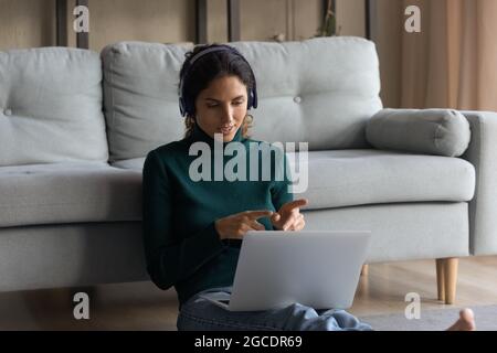 Smiling woman in headphones chatting, using laptop, sitting on floor Stock Photo