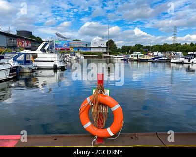 Oberhausen (Centro), Germany - July 9. 2021: View on inland port with boats in summer with orange lifebelt, sealife building background Stock Photo