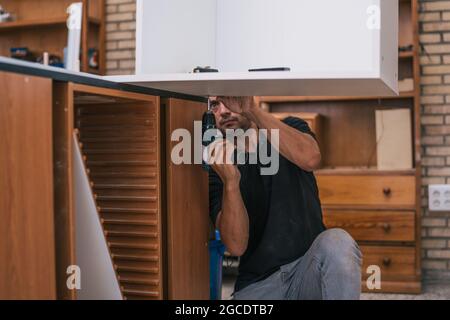 Worker drilling a hole under a board in a workshop. Stock Photo