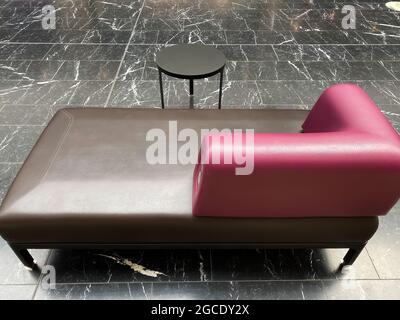 Closeup of one isolated empty purple brown leather chaiselongue with small round table on black and white marble floor Stock Photo