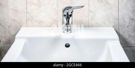 Chromed faucet with lever to mix hot and cold water on a modern white sink in a bathroom with tiled walls. Domestic life and hygiene Stock Photo