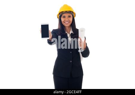portrait of asian engineer woman with helmet holding blueprints and showing blank screen mobile phone isolated white background Stock Photo