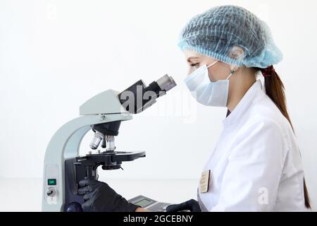 Female scientist looking through microscope in modern chemical laboratory doing some research. Analyzing samples using a microscope Stock Photo