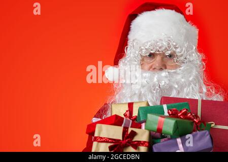 Happy Santa Claus with gift boxes in hands on red background with copy space Stock Photo