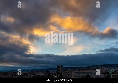 Dark rain clouds are approaching the city and covering the clear blue sky at evening. Clear sky is visible through the gap in the dark gloomy clouds. Stock Photo