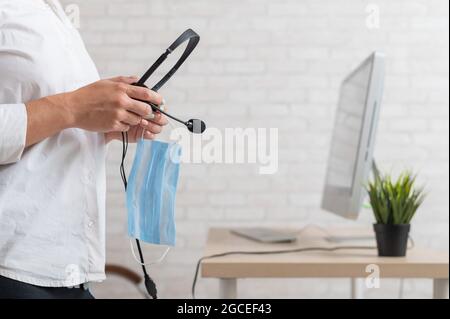 A faceless female employee holds a headset and a face mask. Woman with headphones and a medical mask in her hands Stock Photo