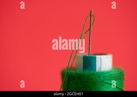 Hand sewing needle and thread close up in red background Stock Photo