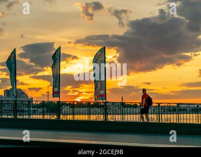 Man walking on Trinity bridge while sun rises painting sky in yellow tints, 4:15 AM, St Petersburg, Russia Stock Photo