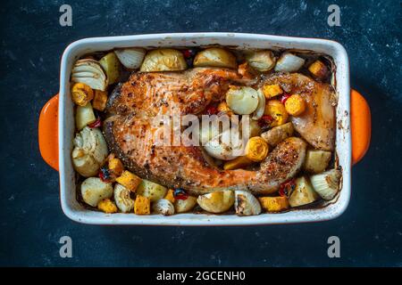 Baked salmon fillet with potatoes, carrots, onions, red peppers and garlic in a ceramic bowl on a black background, close up Stock Photo