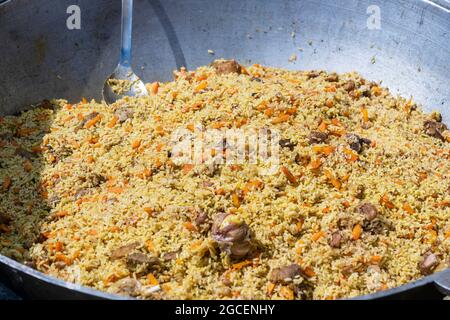 Cooking of traditional pilaf in big cauldron on the street food market in Ukraine, close up Stock Photo