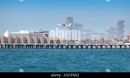 A light twin engine propeller plane takes off from the runway from an artificial island in Dubai. Large construction sites in the background Stock Photo